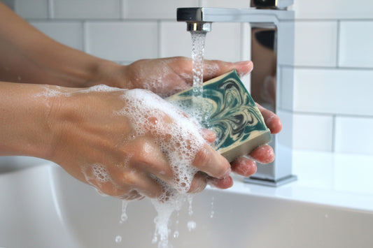 Marbled green and beige soap bar in someone's hands as they wash with a tiled bathroom background