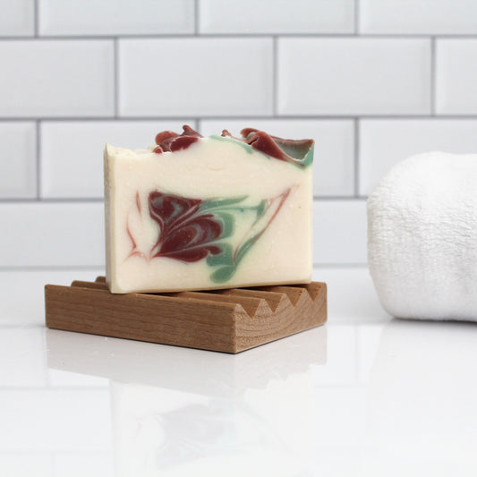 Bar of soap with marbled design on a wooden soap dish against a tiled bathroom wall.
