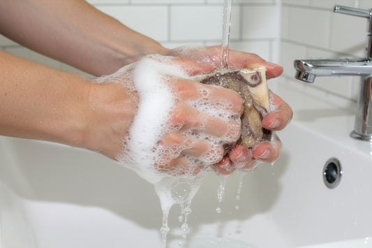 Person washing their hands with a bar of soap under running water in a sink.