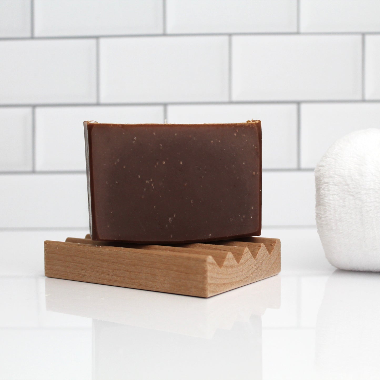 Brown soap bar on a wooden soap dish against a white tiled wall.