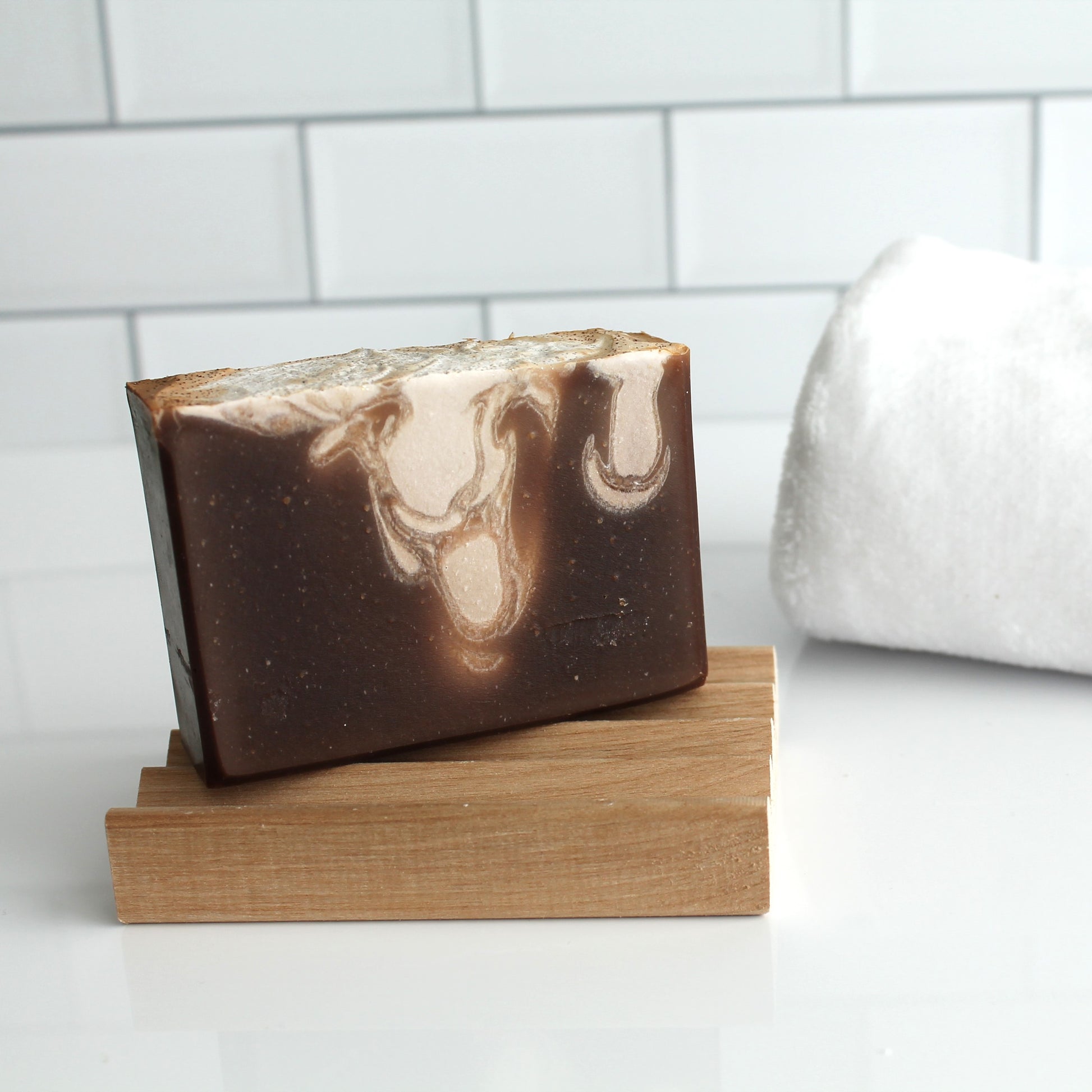 Bar of soap with a marbled design on a wooden stand against a tiled wall background